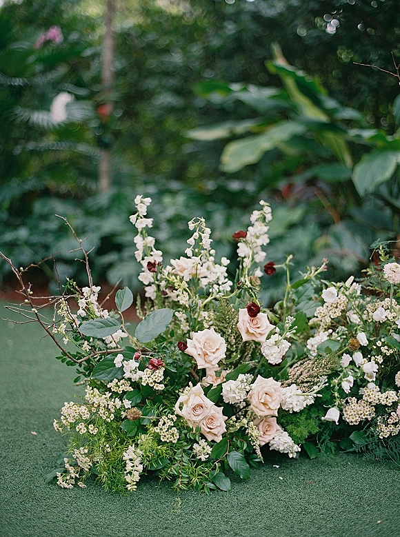 Wedding floral arrangement with blush roses and white flowers, airy greenery and branches, resting on grass amid garden foliage