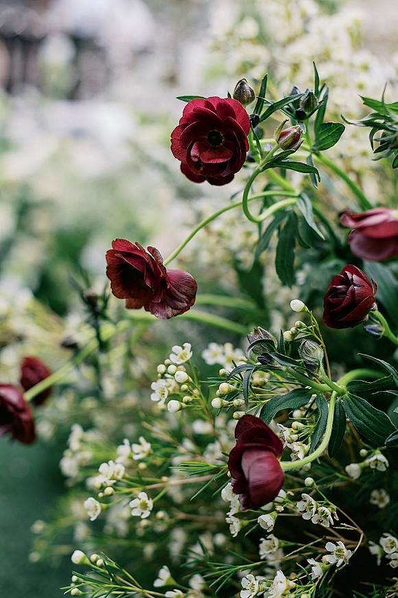 Wedding bouquet with burgundy wedding bouquet blooms, white filler flowers and green foliage, stems visible against a blurred garden backdrop