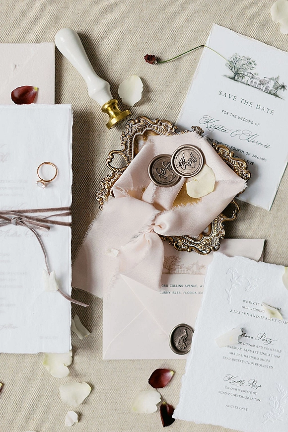 Invitation suite wedding invitation flat lay on linen with deckle edge cards, blush ribbon, vellum envelope, wax seals, ring on brass tray