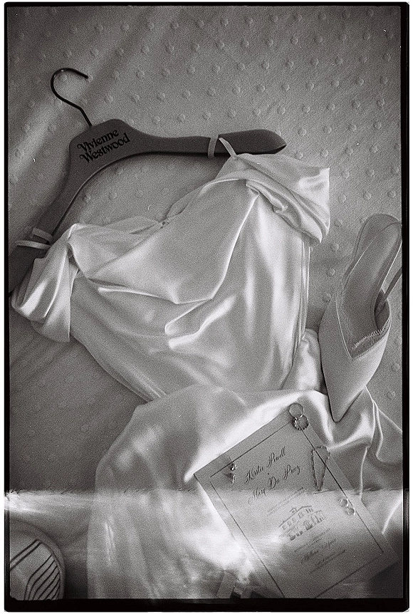 Wedding dress flat lay with satin wedding dress on a wooden hanger, shoes, invitation, pearl jewelry and rings on a textured fabric backdrop