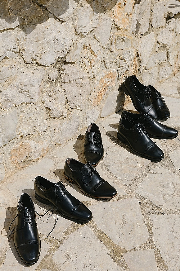 Groom shoes, black wedding shoes with laces resting on sunlit stone steps, casting crisp shadows against a stone wall