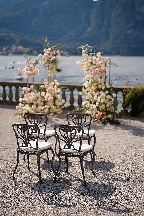 Ceremony setup with outdoor wedding ceremony chairs and pastel floral arrangements on a stone terrace overlooking a lake and mountains