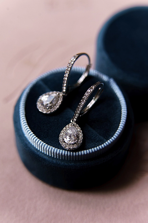 Bridal earrings with teardrop crystal earrings in a blue velvet ring box, featuring halo pavé stones on a pink surface