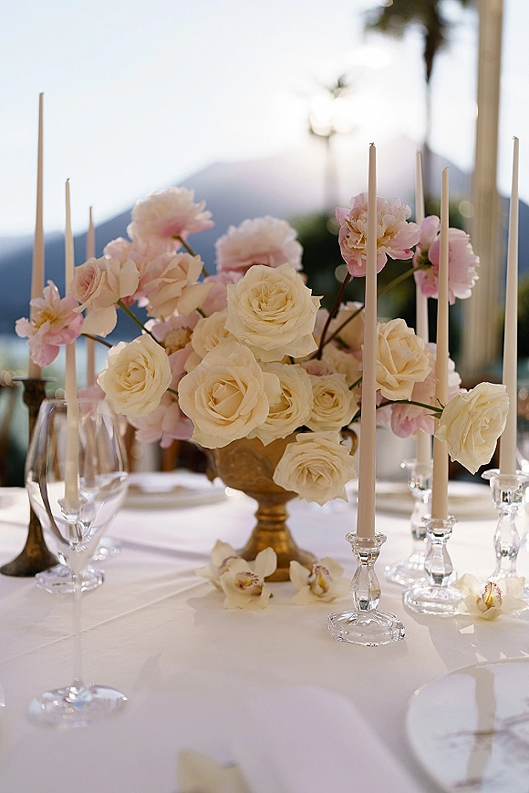 Reception tablescape with wedding centerpiece ideas featuring white roses, blush blooms, taper candles in glass, and gold compote, mountain view backdrop