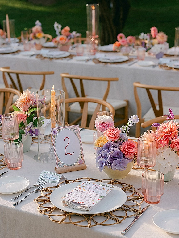 Reception tablescape with outdoor wedding table decor featuring rattan chargers, menus, pastel hydrangea and dahlia florals on a lawn