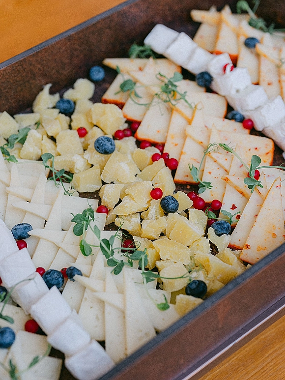 Wedding cheese board with assorted slices and chunks, blueberries and red berries, and pea shoots on a wooden tray atop a wood tabletop