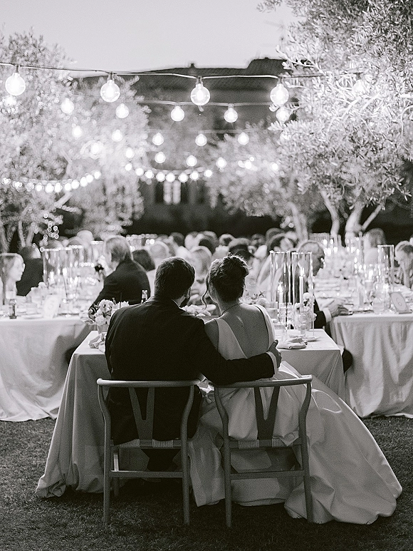 Wedding reception moment under string lights, candlelit tables with floral centerpieces as guests mingle on the lawn at night