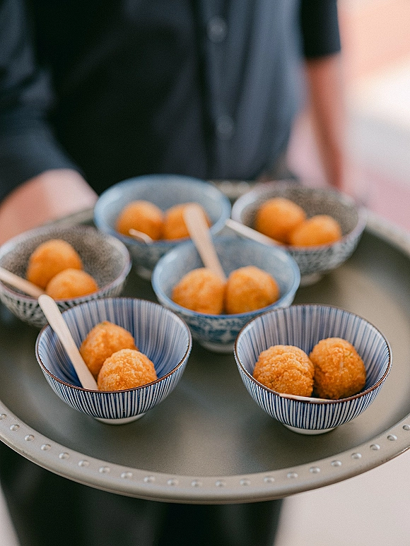 Wedding dessert bites on a passed dessert tray in patterned ceramic bowls with round dessert balls and small wooden spoons, held by a server indoors
