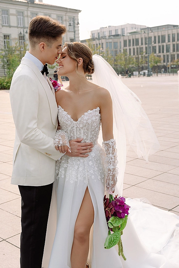 Wedding couple portrait with bride and groom forehead kiss, her cascading orchid bouquet and veil in an urban city plaza with modern buildings