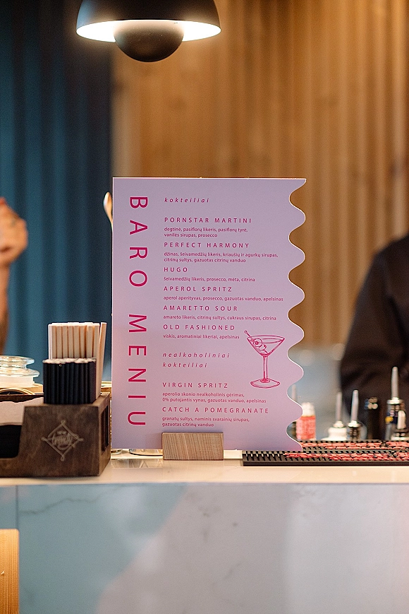 Bar menu sign with wedding bar menu card in a wooden holder on the counter, with straws, bar tools, and wood panel wall backdrop