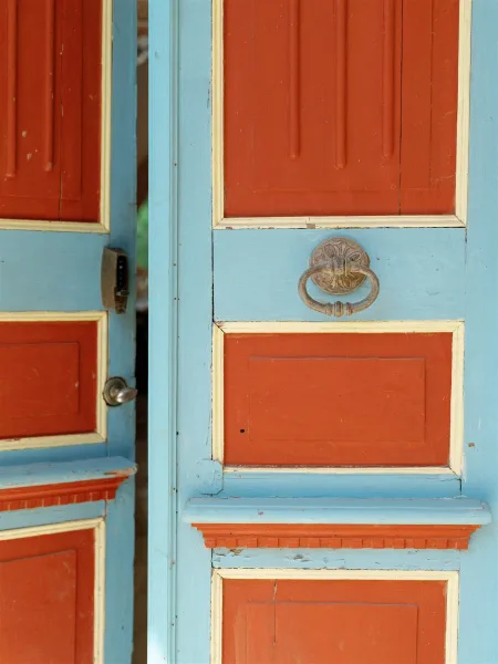 Vintage door detail with an antique door knocker and latch on painted wood panels, peeling paint on the door frame in back