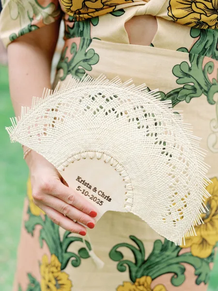 Personalized wedding fan, custom wedding hand fan held with red nail polish, woven straw design against a green wall backdrop