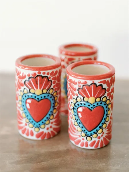 Wedding shot glasses, hand painted shot glasses with heart designs, red rims, and floral patterns arranged on a neutral tabletop against white background