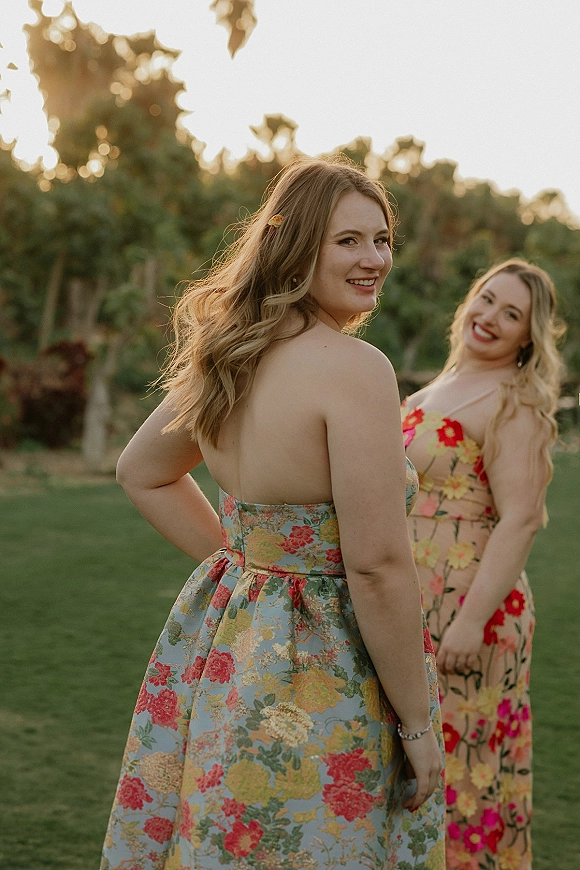 Bridesmaid portraits of two bridesmaids in floral dresses, one strapless, with a hair clip and bracelet on a lawn at sunset