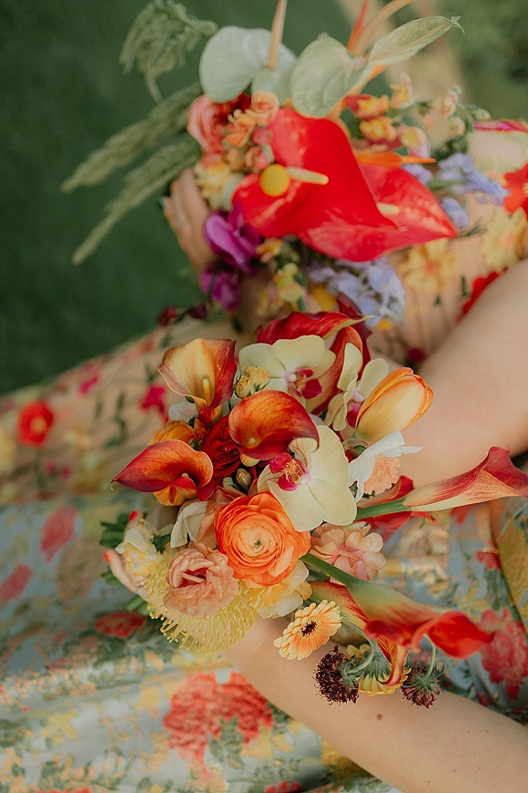 Bridal bouquet with tropical bridal bouquet blooms—calla lilies, orchids, roses and anthurium—tied with ribbon against a green wall