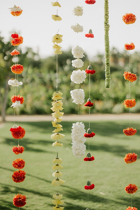Hanging floral decor with marigold flower garland decor and white flower strings forming a curtain backdrop over an outdoor lawn with greenery
