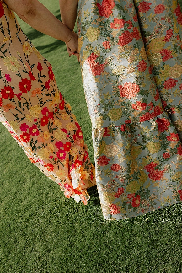 Wedding guest dresses in floral wedding guest dress styles, two long embroidered and brocade gowns shown close-up against a grass lawn