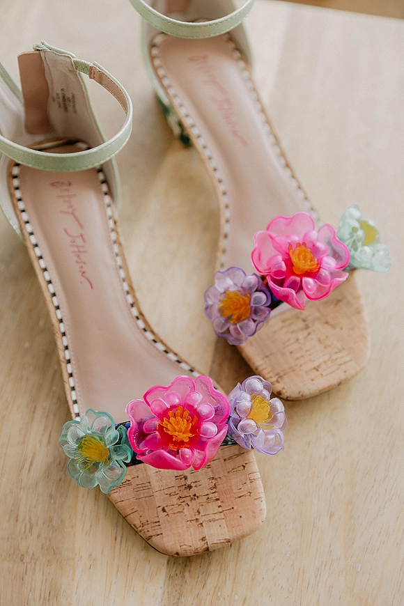 Bridal shoes with wedding sandal heels featuring floral appliques, ankle straps, and cork block heels resting on a wood surface