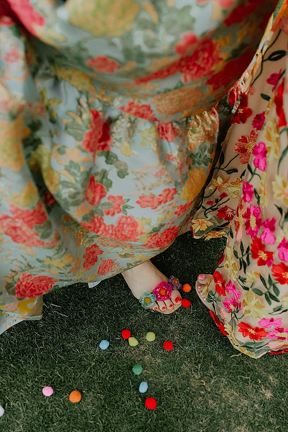 Bridal party fashion with bridesmaid floral dresses as feet in sandals with pom pom clips and confetti pom poms rest on a grass lawn