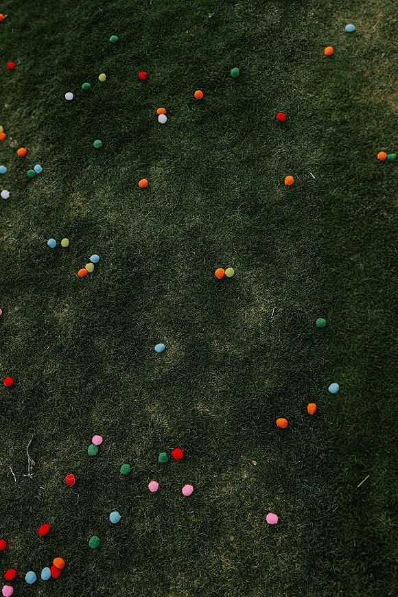Wedding lawn games arranged on a grass lawn with colorful pom poms scattered around for playful outdoor wedding entertainment