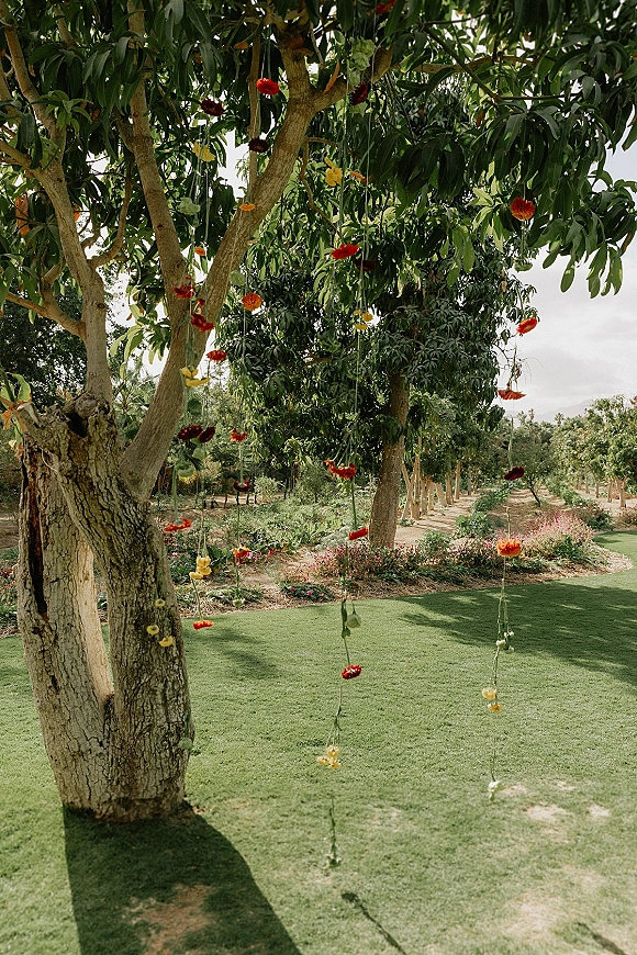 Hanging flower decor with a hanging flower installation of colorful floral strings dangling from orchard tree branches over a garden lawn