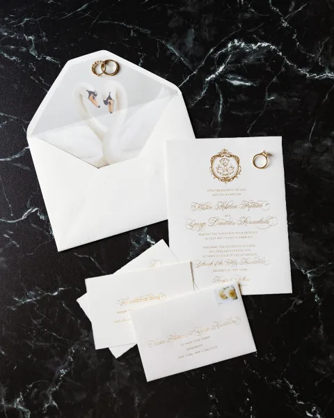 Invitation suite wedding invitation flat lay with envelope, RSVP and insert cards, gold foil lettering, postage stamp, and rings on black marble surface