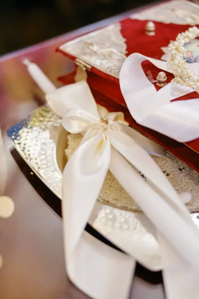Wedding invitation suite in a red velvet invitation box tied with white satin ribbon on a silver tray with lace, pearls, and ivory rice accents
