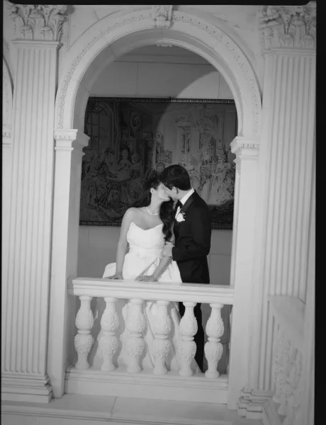 Wedding kiss portrait of bride and groom kissing on a balcony, bride in strapless dress with pearl necklace beside an arched doorway