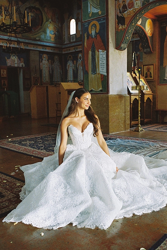 Bridal portrait of a bride sitting on the floor in a strapless lace wedding dress with veil and long train inside an icon-filled church interior