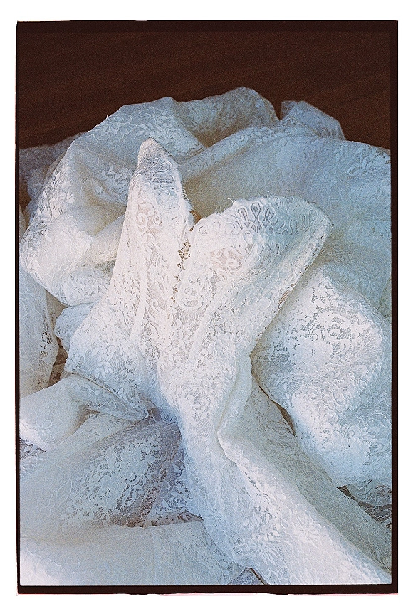 Wedding dress close-up showing lace wedding dress texture with a floral pattern and scalloped edge on a dark surface with soft shadows