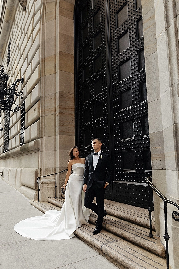 Couple portrait of bride and groom portrait on stone steps, bride in strapless gown with long train leaning on tuxedoed groom by black door