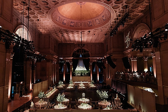 Wedding reception decor with round and banquet tables, white linens, floral centerpieces, candelabras and candles in an ornate grand ballroom