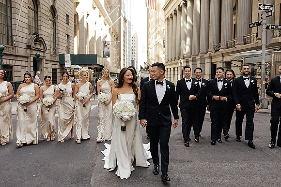 Wedding party portrait with bride and groom walking, bridesmaids in champagne satin dresses and groomsmen in tuxedos on a city street