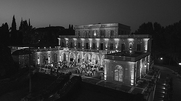 Outdoor wedding reception with villa wedding reception ambiance, round tables with floral centerpieces under string lights on a terrace courtyard at night