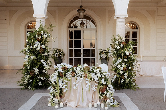 Wedding sweetheart table with sweetheart table flowers, lush greenery and orchids, candlelit on a veranda with white columns and French doors