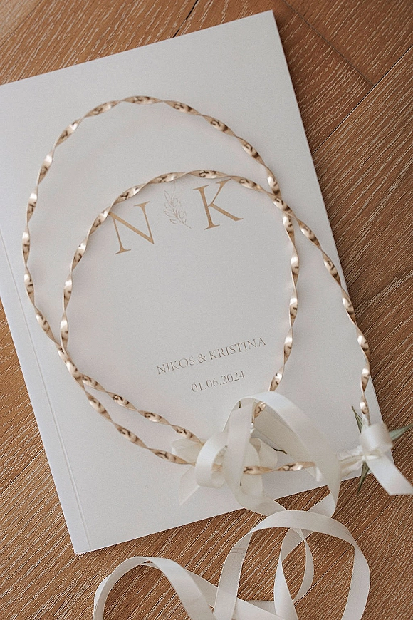 Wedding invitation with gold foil lettering and monogram initials, tied with a white ribbon beside an envelope on a wood floor