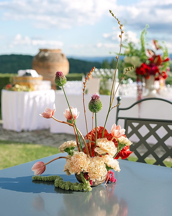 Wedding centerpiece with a low floral centerpiece in a metal bowl, featuring coral anthurium and tulips on a white linen table with mountain views