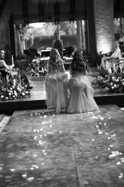 Flower girl processional with two flower girls walking aisle from behind, scattering rose petals on a runner past candles at an outdoor ceremony