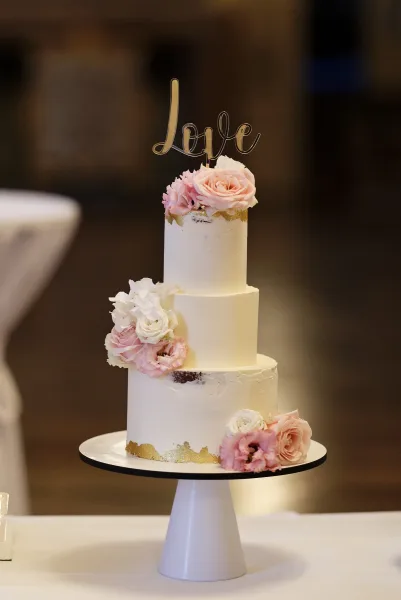 Wedding cake, three tier cake with a smooth white finish, adorned with pink roses cascading down the tiers.