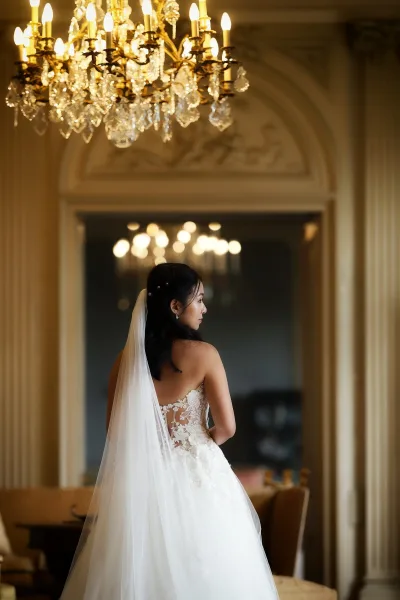 Bridal portrait in a wedding dress back view, the bride gazes away with loose waves, framed by an arched doorway beneath a crystal chandelier.