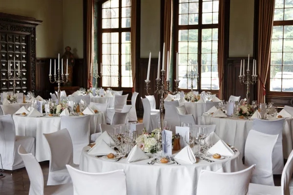 Reception tablescape in ballroom reception decor, centered by silver candelabras, set before tall windows and wood-paneled walls.