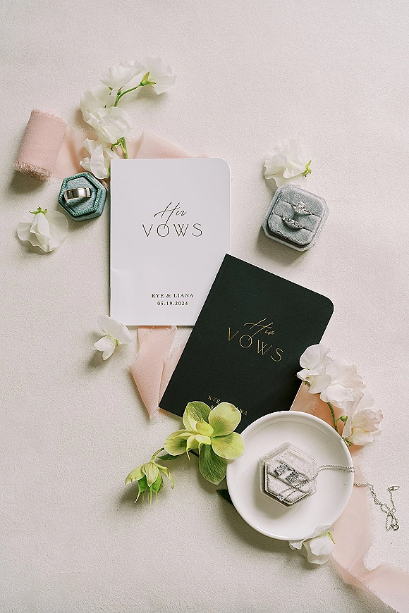 Wedding vows books with vow booklets and wedding rings in velvet ring boxes, styled with a blush ribbon on light fabric surface