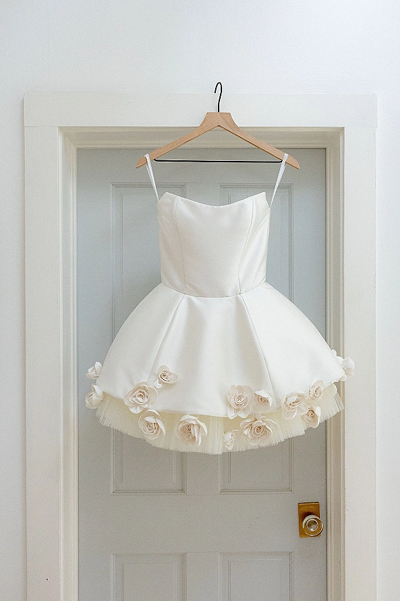 Wedding dress on a wooden hanger, a short tea length wedding dress with spaghetti straps, 3D floral appliqués and tulle hem by a doorway