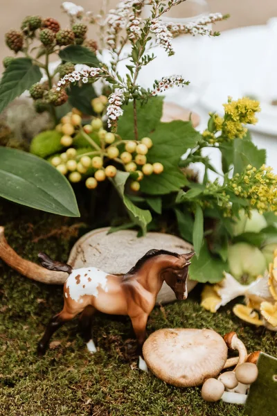Wedding tablescape with woodland wedding tablescape details, moss runner, wildflowers, berries, mushrooms, and a horse figurine on tabletop