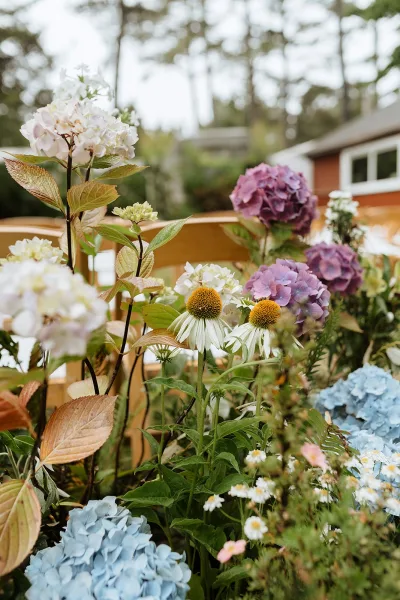 Wedding florals featuring hydrangea wedding flowers and wildflower accents spilling along a wooden railing in an outdoor garden by the house
