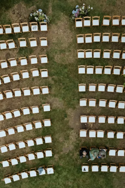 Ceremony seating with wood folding chairs and white cushions arranged in rows beside an aisle runner on a green grass lawn