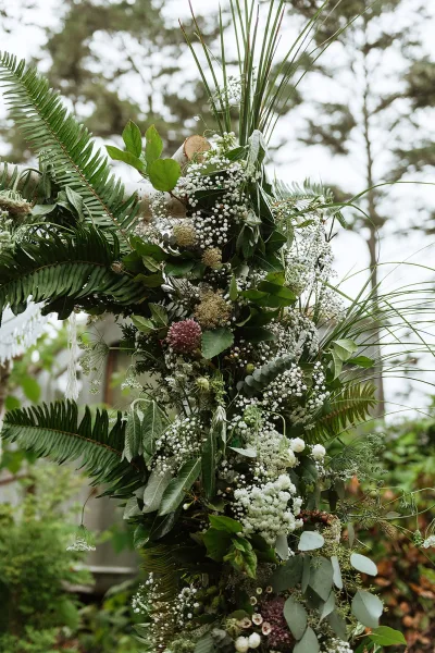 Wedding altar flowers on a ceremony arch greenery design with ferns and baby's breath, set against garden trees and open sky
