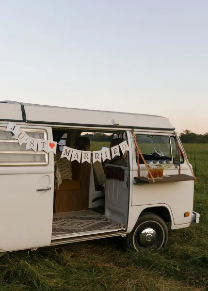 Wedding getaway car with a just married banner, paper bunting, and drink station set up at the back in a grassy field under open sky