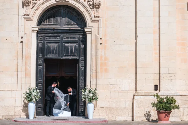 Church entrance flowers create elegant ceremony entrance decor in white urn vases by a stone facade and arched wooden doors.