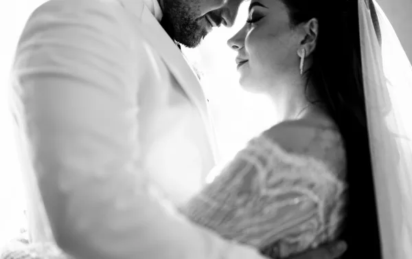 Couple portrait of a bride and groom embrace, foreheads touching, her bridal veil framing them as they share an intimate, tender moment.